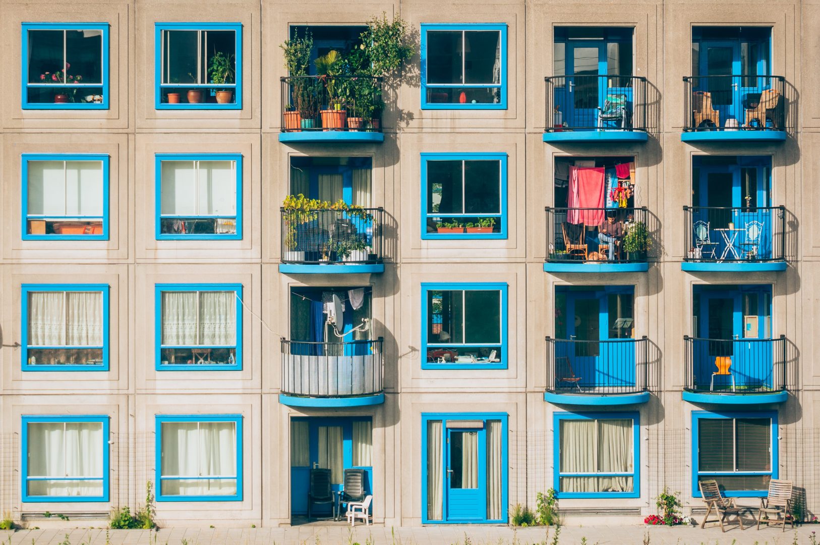 Fassade eines Mehrfamilienhauses mit hübschen blauen Fenstern und bepflanzten Balkonen.
