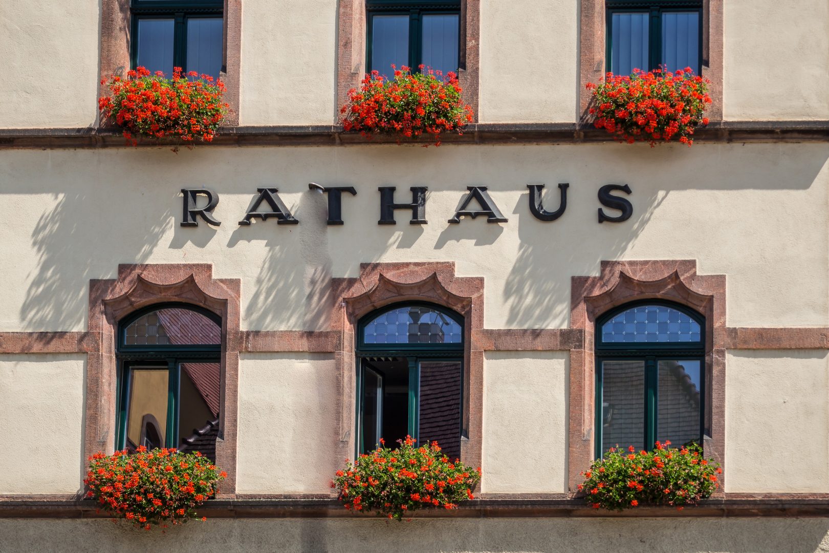 Außenansicht eines Rathauses mit rotenGeranien vor dem Fenster