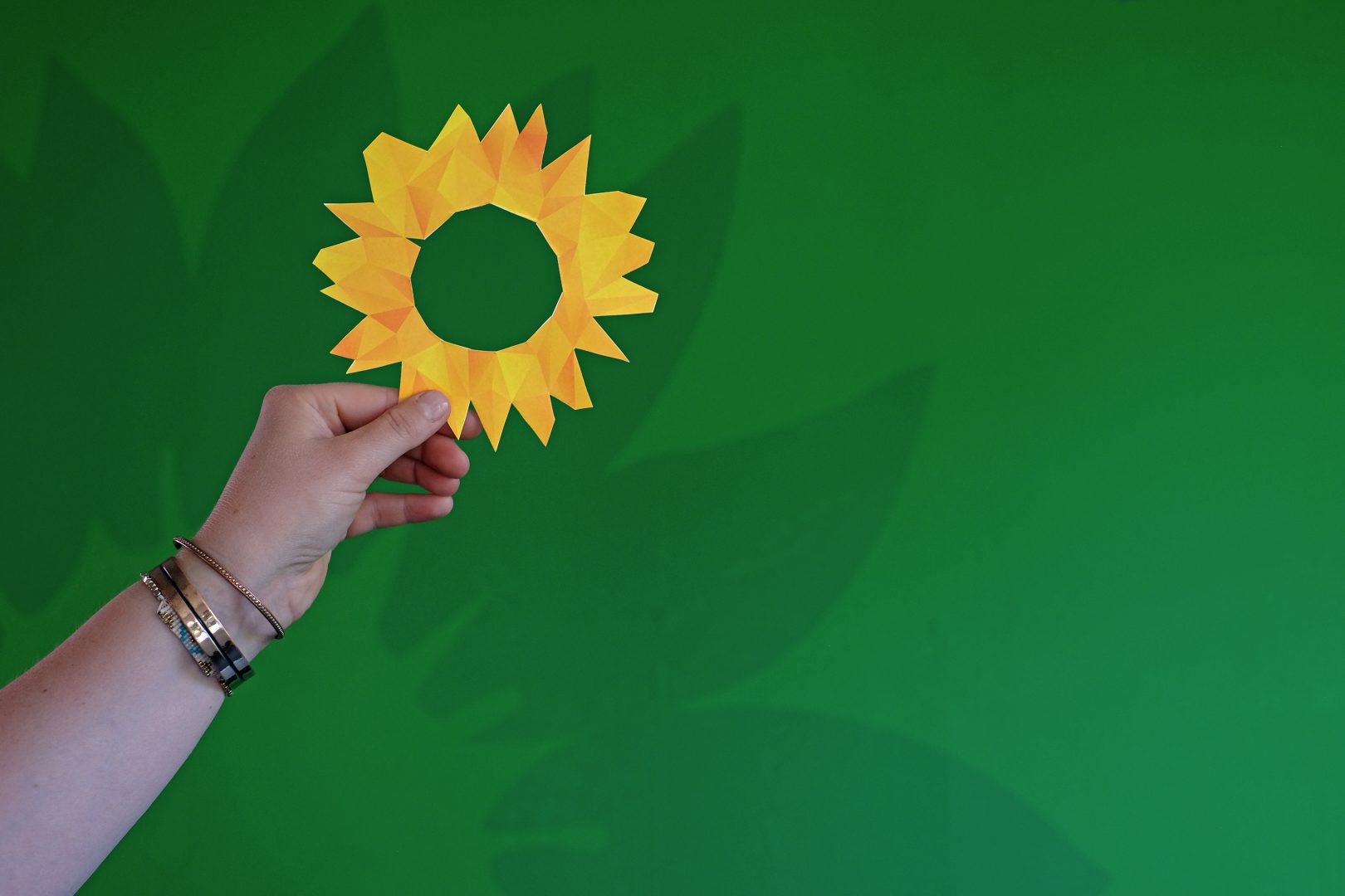Eine ausgeschnittene Sonnenblume in Pixel-Optik wird von einer Hand vor einen grünen Hintergrund gehalten