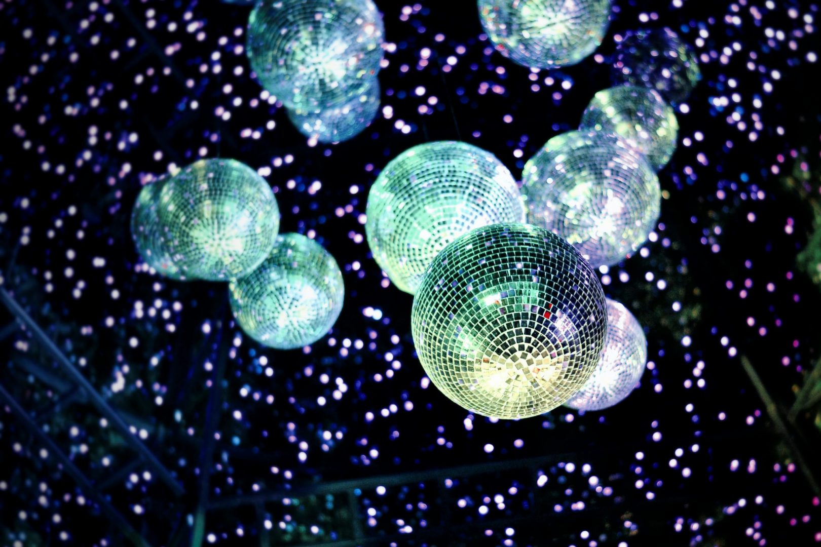 Zahlreiche glitzernde Discokugeln hängen von der Decke einer Kulturlocation und werfen viele kleine Lichtpunkte in den dunklen Raum