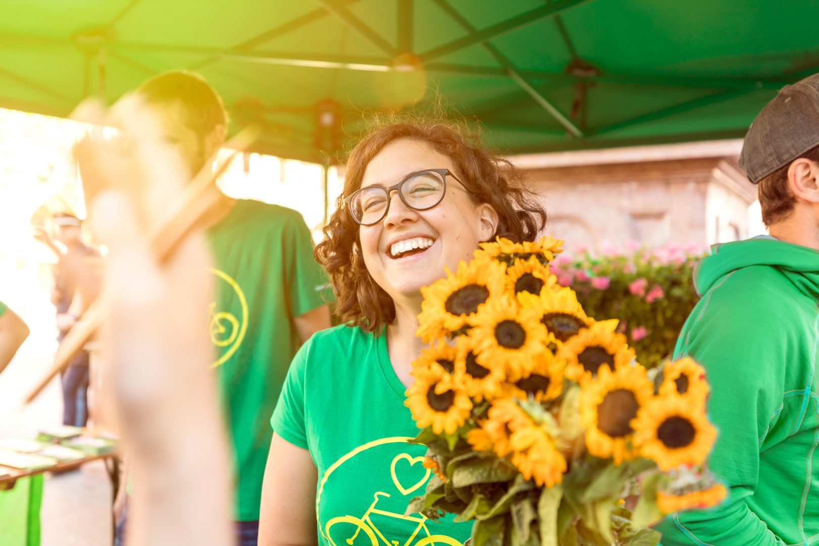 Grüne Mitglieder am Wahlkampf-Stand. Im Mittelpunkt des Bildes eine lachende junge Frau, die einen Strauß Sonnenblumen hält