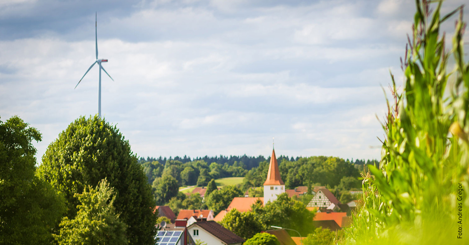 Ein bayerisches Dorf mit Kirchturm, Windrad und Solaranlagen im Sonnenschein